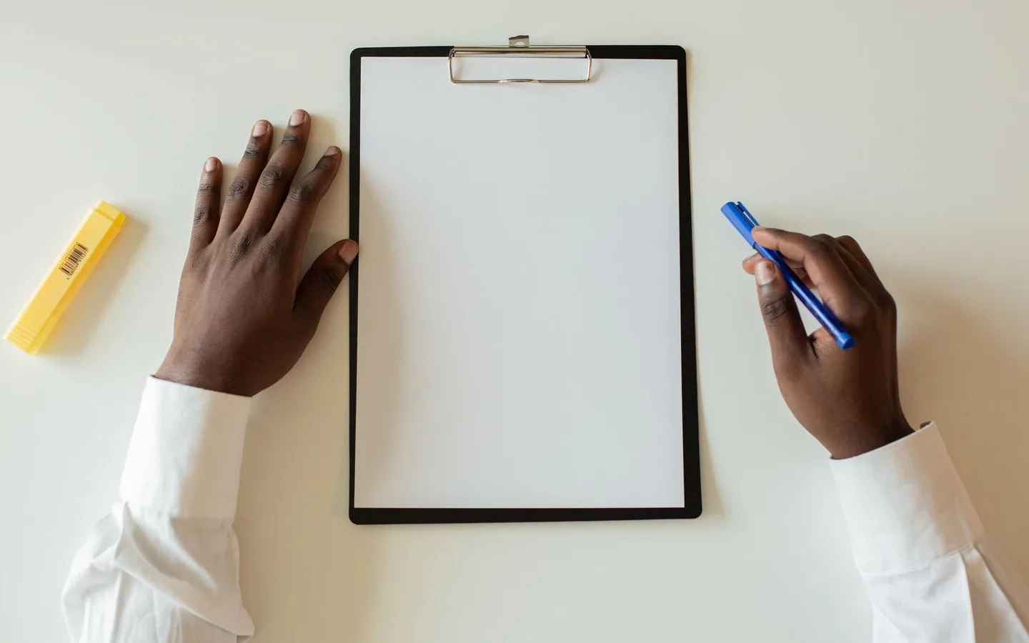 Hands holding a clipboard and pen above a white desk.